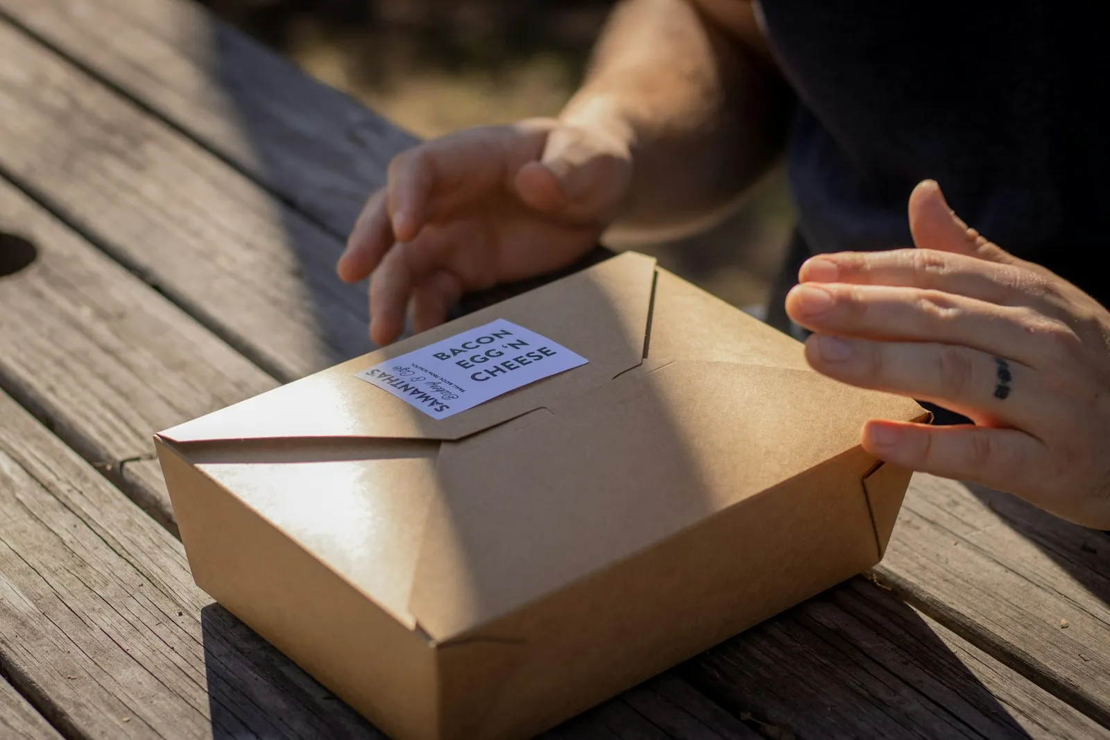 One person handing a box of food to another across a wooden table